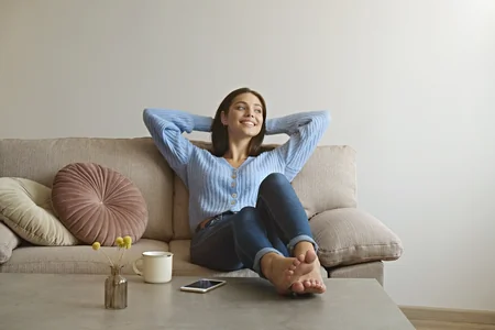Relaxed smiling woman with hands behind her head sitting on a couch